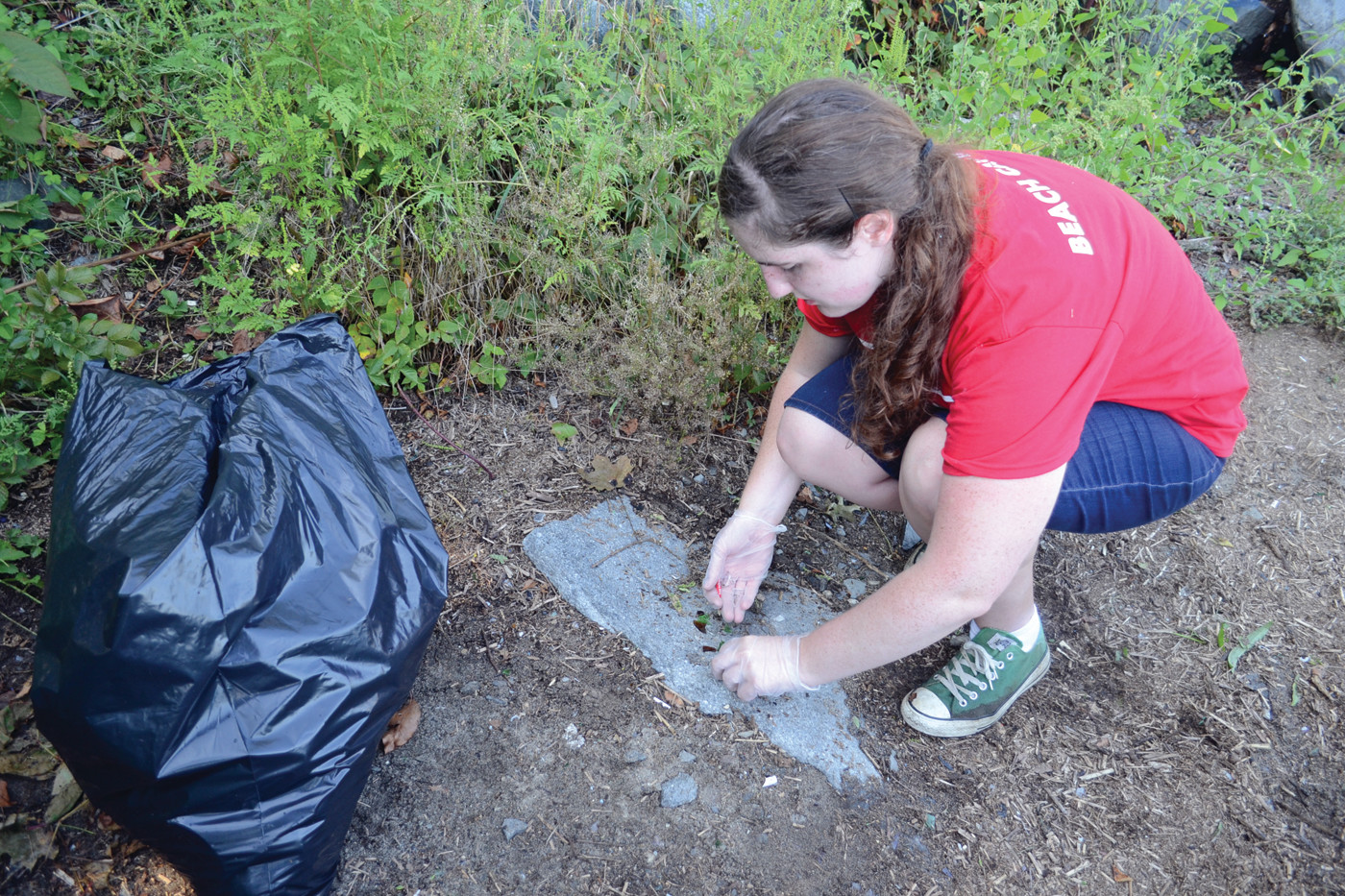 EVERY LITTLE BIT MATTERS: Debbie Woolley, working as part of a volunteer management coordinator internship with Save the Bay, picks up little shards of glass off a walking path at Salter Grove.